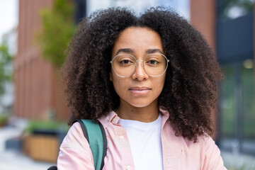 A young black woman, sporting curly hair and glasses, gazes directly at the camera, conveying a sense of calm confidence.