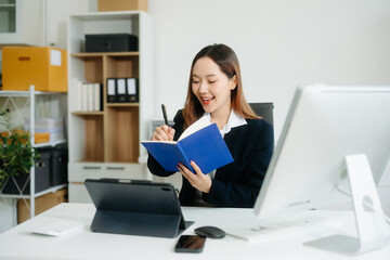 Young Asian businesswoman smiling and working with tablet and laptop in office.