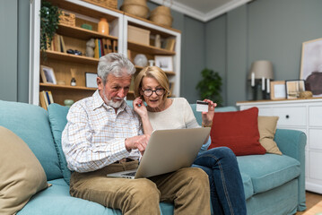 Senior couple, man and woman, using laptop computer and bank credit card for online shopping and...