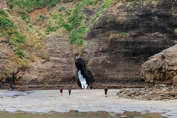 Tourists explore the unique rock formations and keyhole at Piha Beach, Auckland, New Zealand....