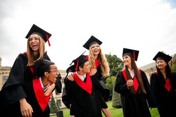 Group of young graduates in traditional caps and gowns celebrating outdoors, enjoying a sunny...