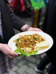 Woman’s hand serving fried noodles with pickles and crackers — a classic Indonesian comfort dish. South Jakarta, Indonesia - June 1, 2017