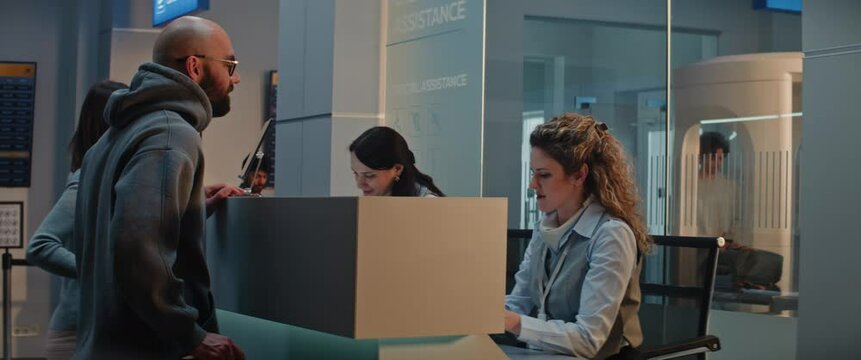 International Airport Terminal: Woman Giving Passport and Flight Ticket for Boarding, Young Man Talking with Female Airline Worker at Airport Check-in Counter. Security Checkpoint in the Background.