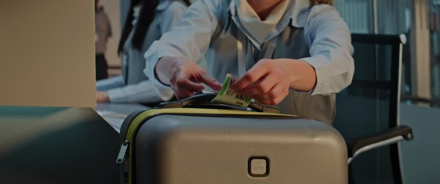 Airport Check-in Counter: Close Up of Female Airline Worker Putting Luggage Tag Sticker on Suitcase for Boarding Flight. Customer Service and Security Baggage Check in International Airport Terminal.