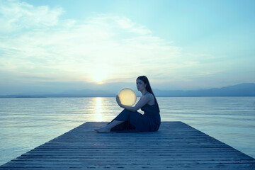 woman in elegant dress holds moon lamp as the setting sun lights it up with magic