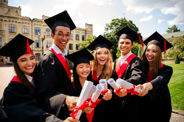 Portrait of group students hold touch diplomas mortarboard gown graduation university building...