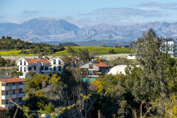 Obraz premium Peaceful spring view of Ilıca village with modern houses and mountain backdrop under a clear sky. Ilıca, Antalya, Turkey.