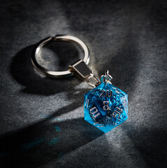 Metal keychain with a blue dice with an image of octopus tentacles on a gray textured background.