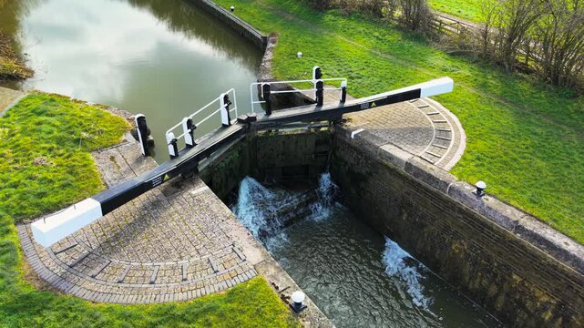 Aerial view canal lock in operation. Overhead shot sluice gate releasing water. Top-down perspective hydraulic lock managing levels. High-angle frame navigational barrier controlling flow
