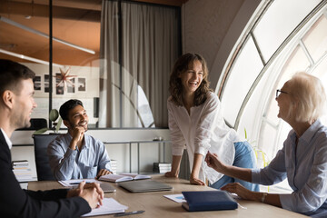 Happy young female boss laughing with coworkers in friendly business meeting board room discussion. CEO manager leader developing project solutions with business international professional colleagues