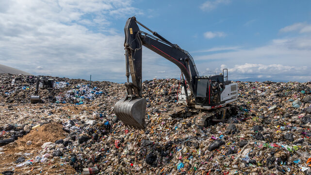 Bulldozer working on massive lanfill waste site with mountain background, Heavy machinery manage plastic waste at larg garbage dump, Excavtor at landfill global waste crisis concept.