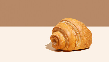 Fresh croissant on yellow and brown background with shadow.