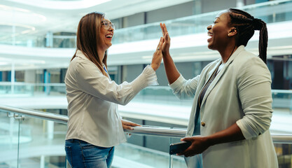 Fototapeta premium Two female colleagues sharing a high five in modern office
