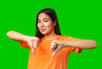 Young woman expressing disappointment with thumbs down gesture against a bright green background