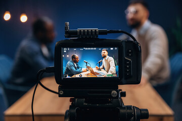 Close up view of camera that is filming. Two radio presenters recording an audio broadcast in a...