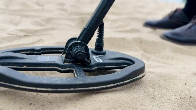 Man scanning sandy ground with metal detecting equipment