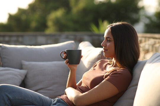 Woman relaxing drinking coffee sitting in exterior sofa in a terrace