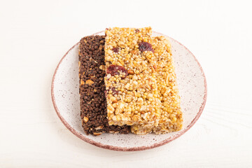 granola bars with caramel, nuts, flakes in ceramic plate on white wooden. Side view, close up.