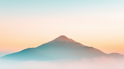 Obraz premium A serene mountain peak rises softly through a gentle mist during sunrise, creating a peaceful and tranquil atmosphere in a picturesque landscape scene.