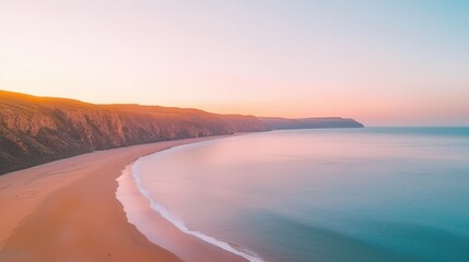 Fototapeta premium Stunning aerial view of a serene coastline at sunset, showcasing gentle waves lapping against the sandy beach, surrounded by lush cliffs under a colorful sky.