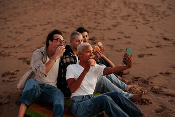 Friends eating donuts and taking a photo of themselves on beach at sunset