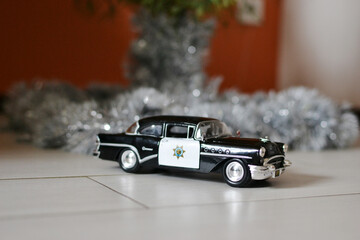 Vintage police car toy model on floor near Christmas decor. © SolaruS