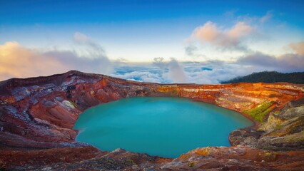 A large blue lake sits in the middle of a rocky mountain. The sky is clear and the sun is setting, casting a warm glow over the scene. The lake is surrounded by a rocky landscape
