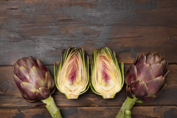 Half and whole purple raw roman artichokes on a dark wooden table top view. Fresh italian vegetables