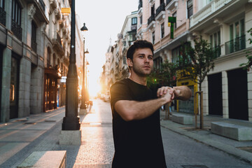 Man preparing for workout with dynamic arm stretch during sunrise in empty street. Morning calmness...