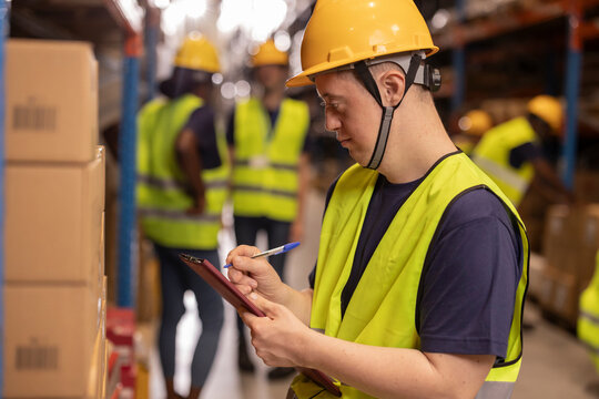 Young warehouse worker with down syndrome checking inventory using clipboard
