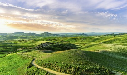 Picturesque landscape of summer green hills under a beautiful sunset sky with clouds. Wildflowers on a green grass meadow. European hills and meadows, Italy.