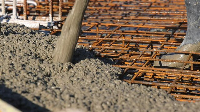 Construction workers with concrete boom pump crane at construction site pouring concrete into a formwork with reinforcement for building a new house, slow motion