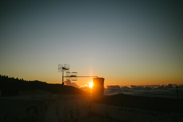 Sunset above the clouds in the mountains. Bright sunlight breaks through fluffy clouds. Old rooftops and vintage metal TV antennas in the foreground.