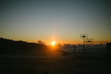 Sunset above the clouds in the mountains. Bright sunlight breaks through fluffy clouds. Old rooftops and vintage metal TV antennas in the foreground.