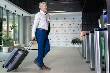Bearded man walking in airport terminal carrying suitcase