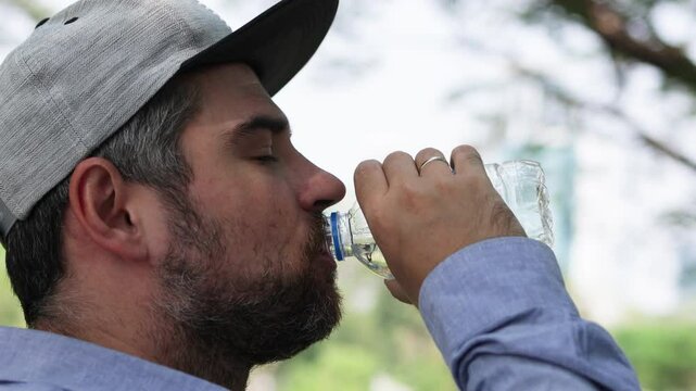 Bearded man in cap drinks water from bottle.