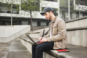 Obraz premium College male student working on laptop sitting on university campus steps