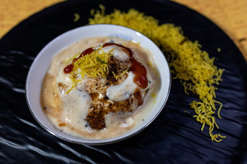 A flavorful Indian chaat dahi vada or dahi bhalla served with yogurt, tamarind chutney, and crispy toppings served on elegant black platter. Ideal for showcasing traditional cuisine and tasty snacks.