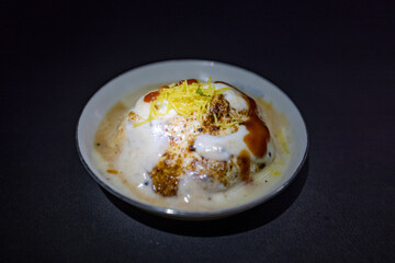 A flavorful Indian chaat dahi vada or dahi bhalla served with yogurt, tamarind chutney, and crispy toppings served on elegant black platter. Ideal for showcasing traditional cuisine and tasty snacks.