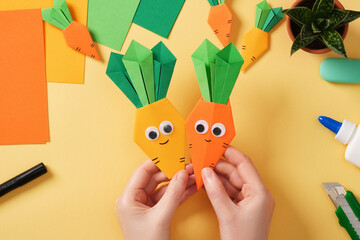 Making a simple origami Easter craft. Hands hold finished crafts of smiling carrots. Around the...