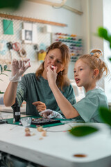 Fototapeta premium Girl carefully fills silicone mold with epoxy resin, adding tiny colorful beads with wooden stick. Craft table is covered with tools, pigment bottles, and UV lamp for hardening resin.