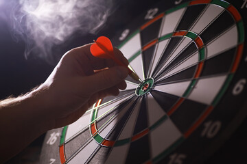 Close-up of Hand Aiming Dart at Bullseye on Dartboard in Smoky Ambient Light