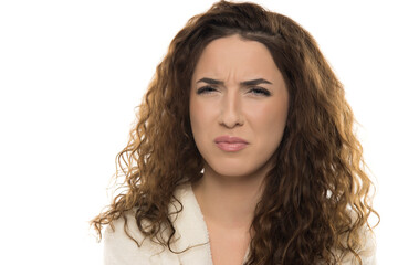 Woman with curly brown hair in white bathrobe showing disgusted expression against white...