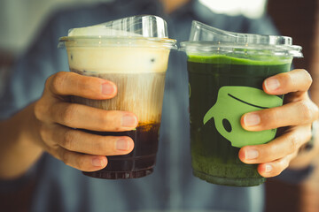 Hands of teenage girl holding glass of ice coffee and ice match green tea together at cafe.