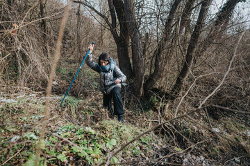 A person walks through a forested area on a cool winter day, utilizing a hiking stick for support and stability.