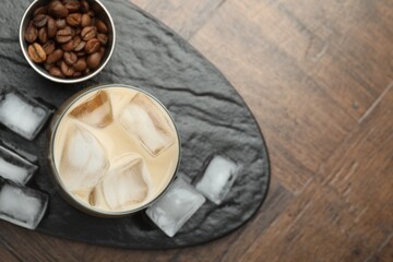 Coffee cream liqueur in glass, ice cubes and beans on wooden table, top view. Space for text