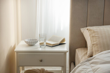 Bedside table with book, bowl and glass of water near bed in room © New Africa