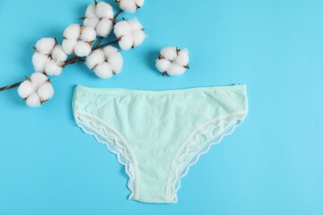 Women's underwear. Beautiful panties and cotton flowers on light blue background, flat lay