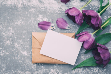 Overhead view of a blank card on a brown envelope tied with string next to a bunch of purple tulips on a table