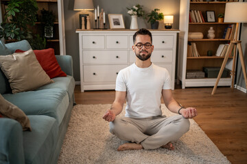 Young man meditating in lotus position at home on carpet